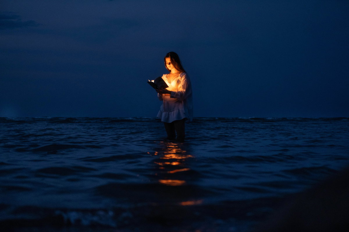 Frau steht im Meer und liest ein Buch