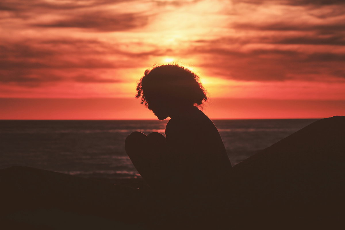 Frau sitzt beim Sonnenuntergang am Meer