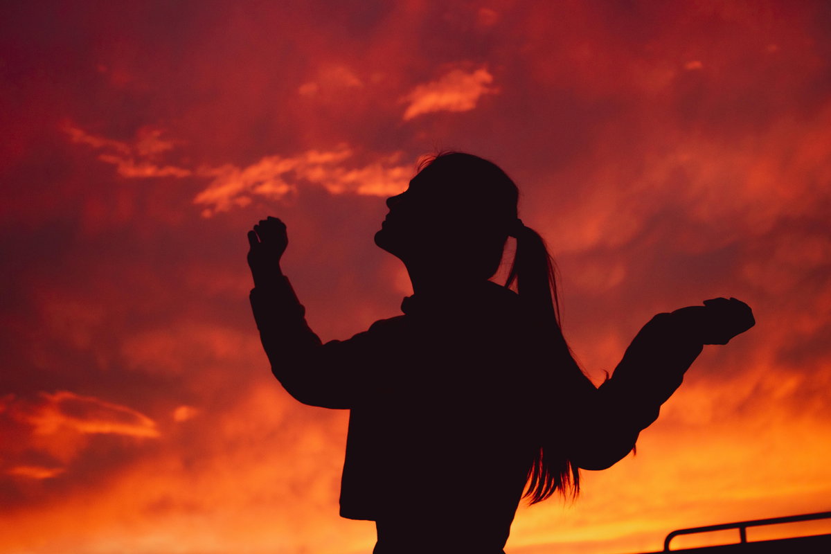 Silhouette einer Frau mit Zopf vor einem roten Himmel