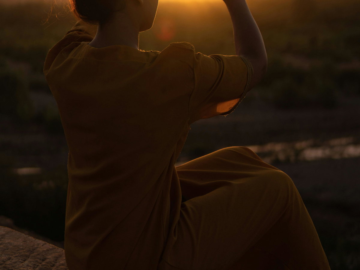 Frau macht Herz mit Händen vor Sonnenuntergang