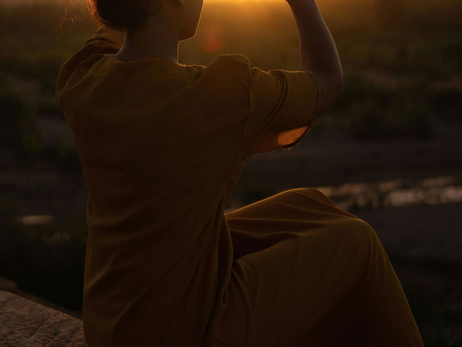 Frau macht Herz mit Händen vor Sonnenuntergang