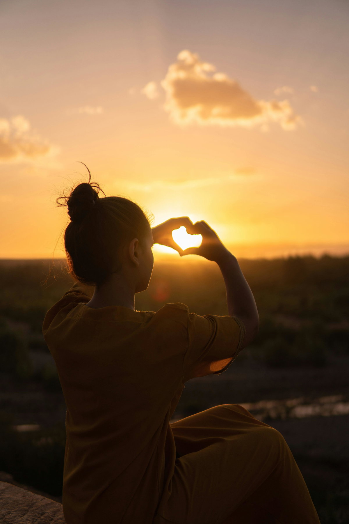 Frau macht Herz mit Händen vor Sonnenuntergang