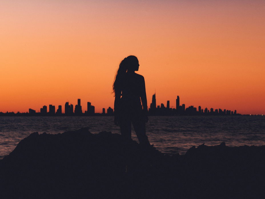 Frau steht vor einer Skyline während des Sonnenuntergangs