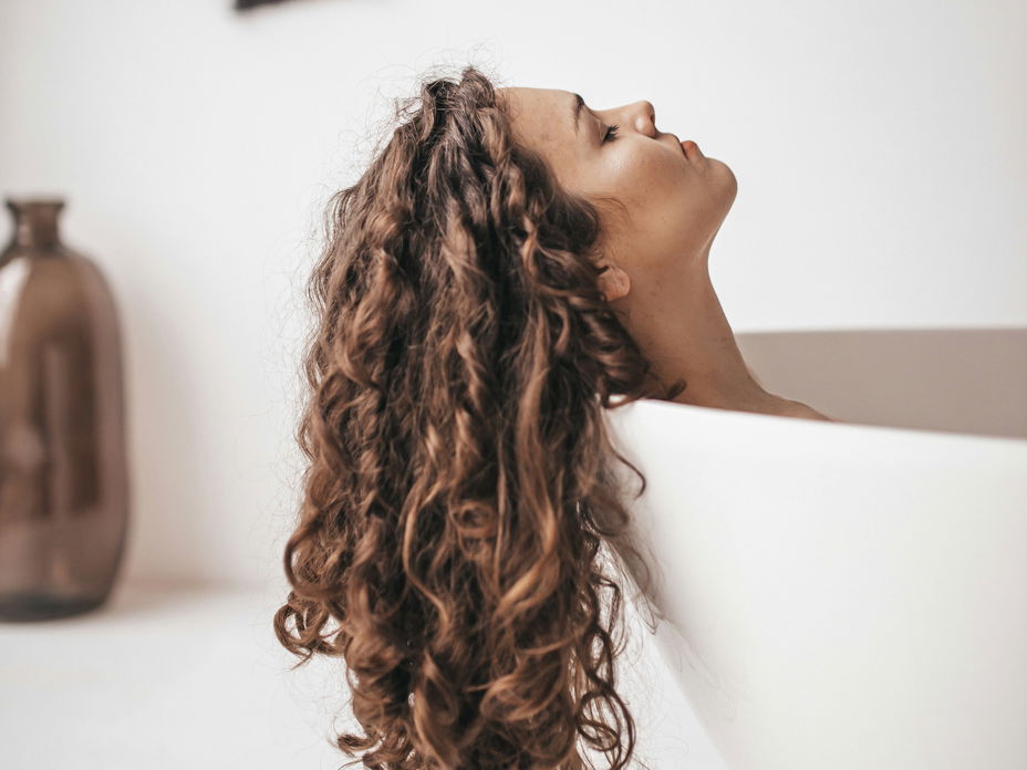 Dicke Haare: Frau liegt in Wanne mit braunen Locken