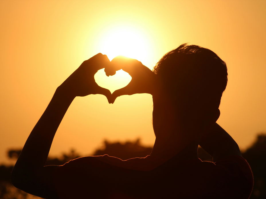 Person zeigt Herz vor Sonne