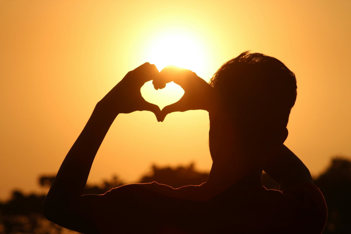 Person zeigt Herz vor Sonne