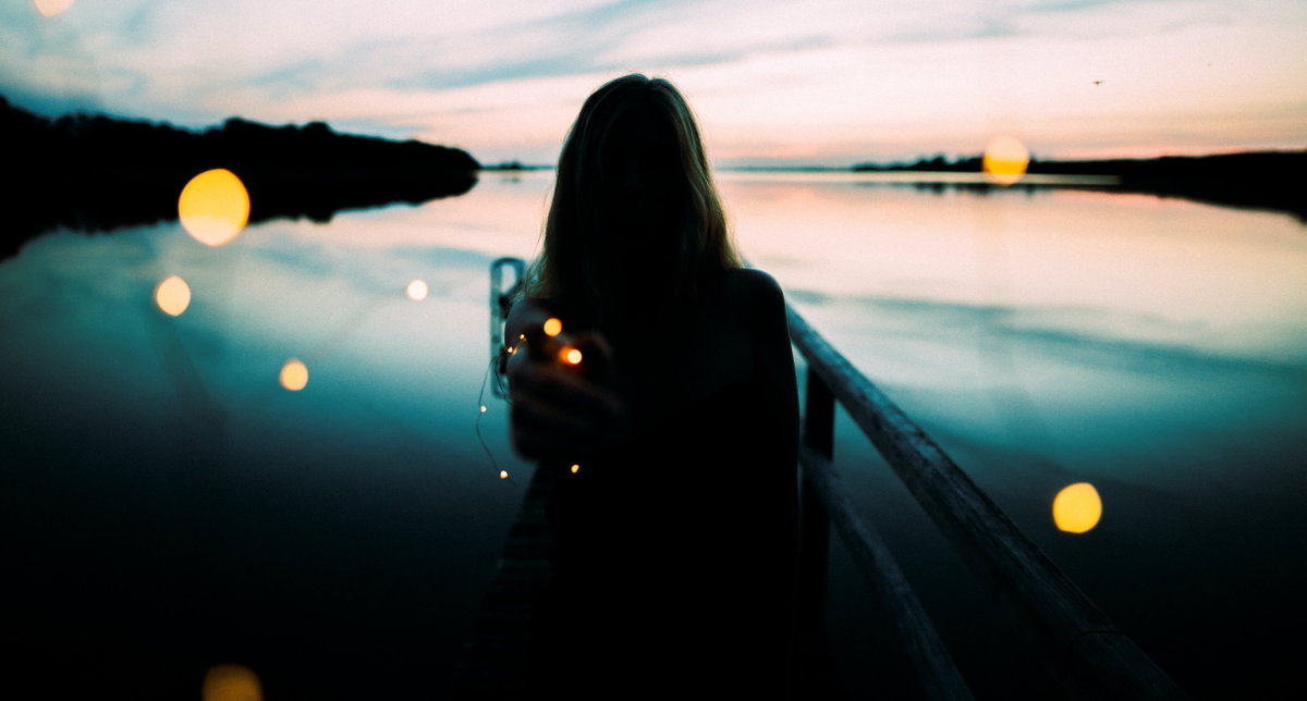Frau steht am See mit einer Lichterkette