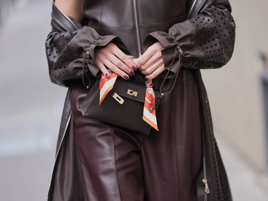 Eine Frau trägt ein braunes Outfit und hält vorn ihre Tasche mit den Fingern fest.