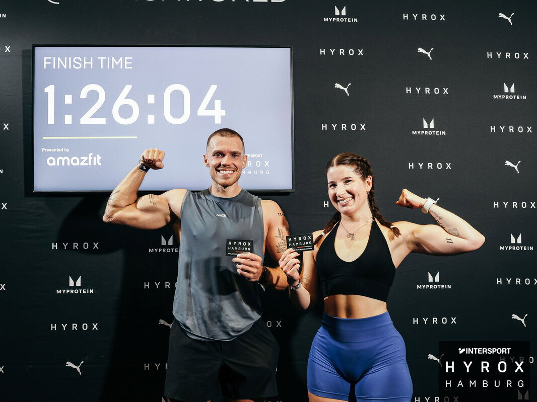 Eine Frau und ein Mann mit Hyrox Patches vor ihrer Finish-Zeit.