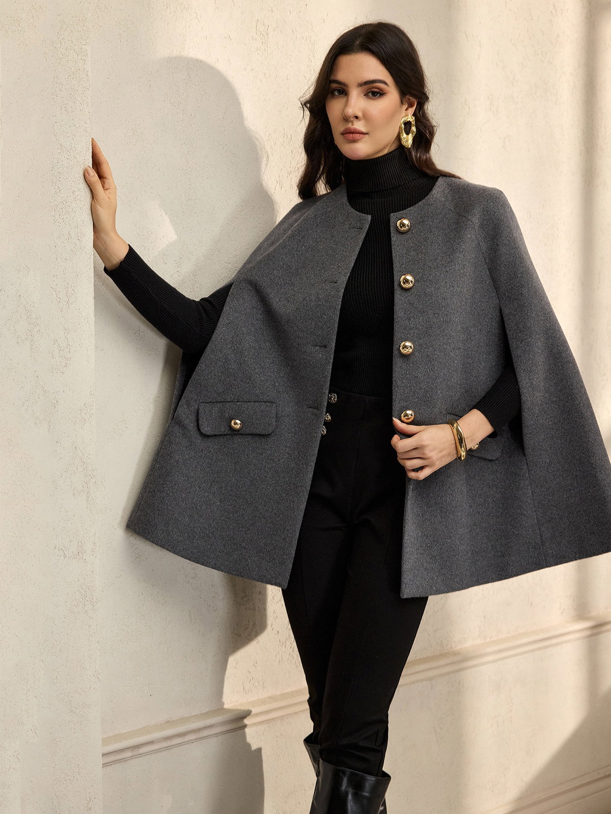 Eine junge Frau mit einem schwarzen Langarmshirt, schwarzer Hose und einem grauen Cape darüber.
