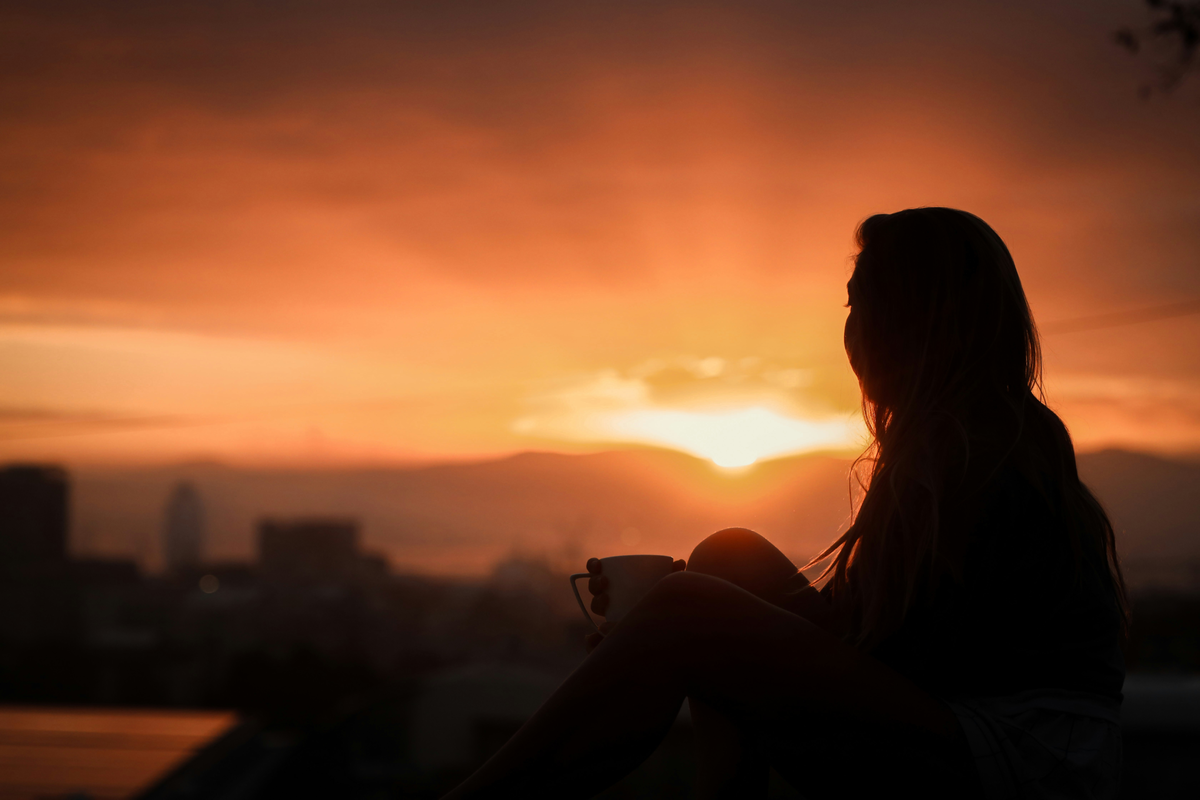 Frau sitzt vor Abendhimmel
