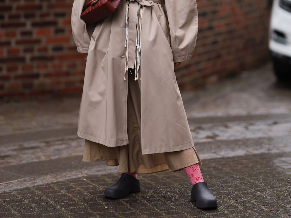 Frau im beigen Mantel mit Garden Shoes und einer weinroten Tasche.