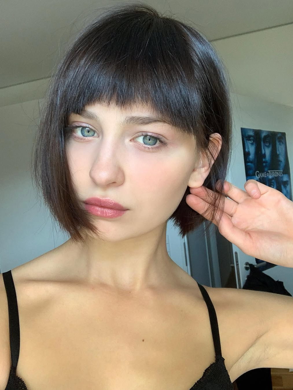 Eine junge Frau mit einem kurzen Bob mit Pony und grünen Augen.