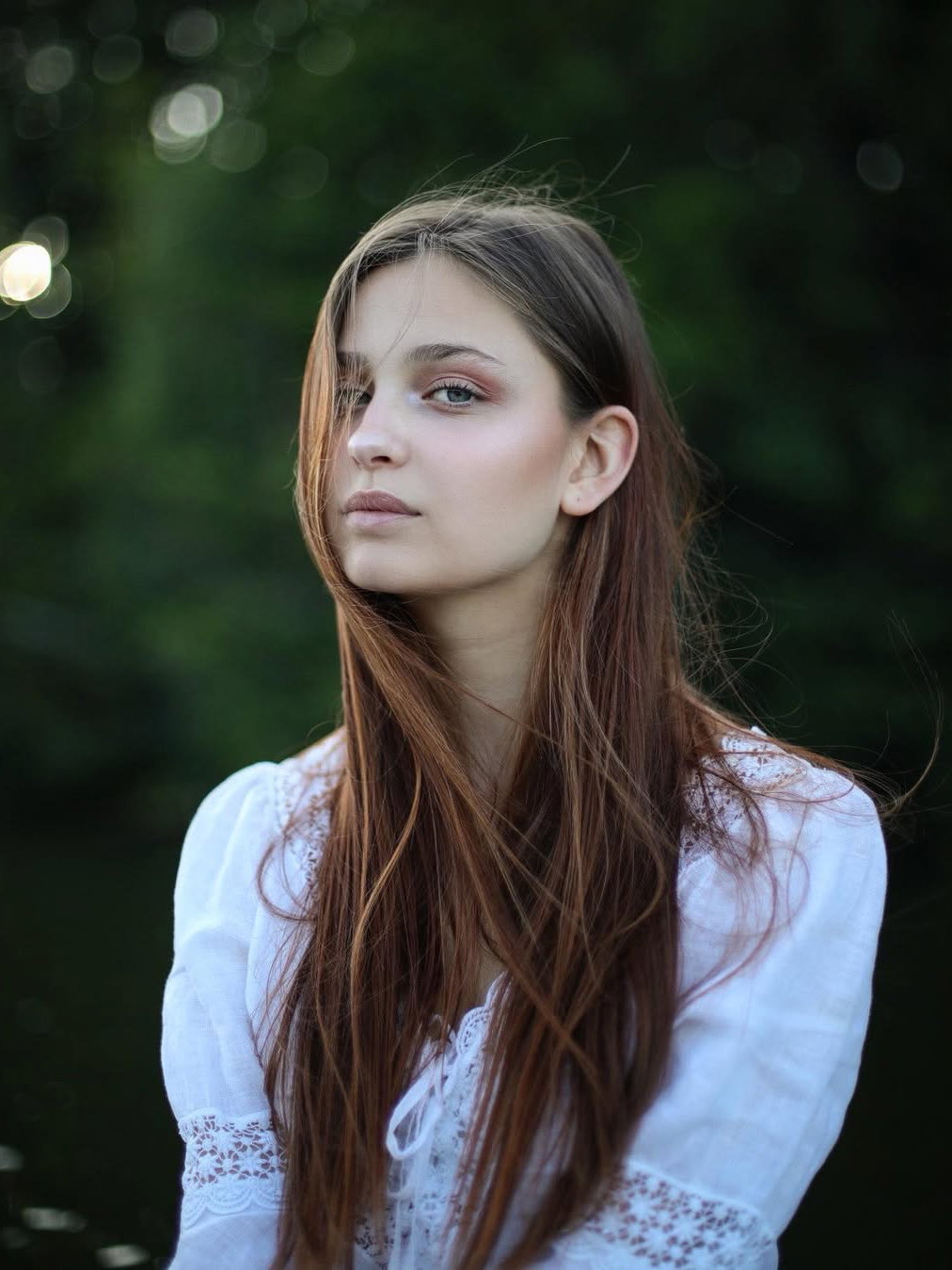 Eine junge Frau mit langen braunen Haaren und einer weißen Bluse mit Spitzeneinsätzen.