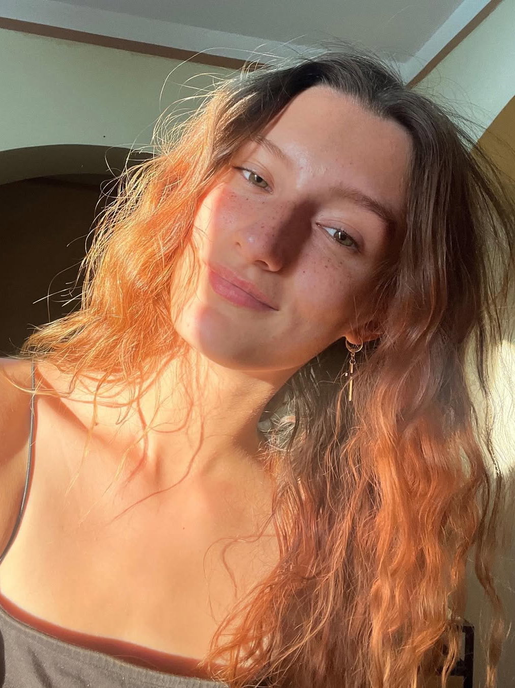 Eine junge Frau mit welligen Haaren, Sommersprossen und Sonne im Gesicht.