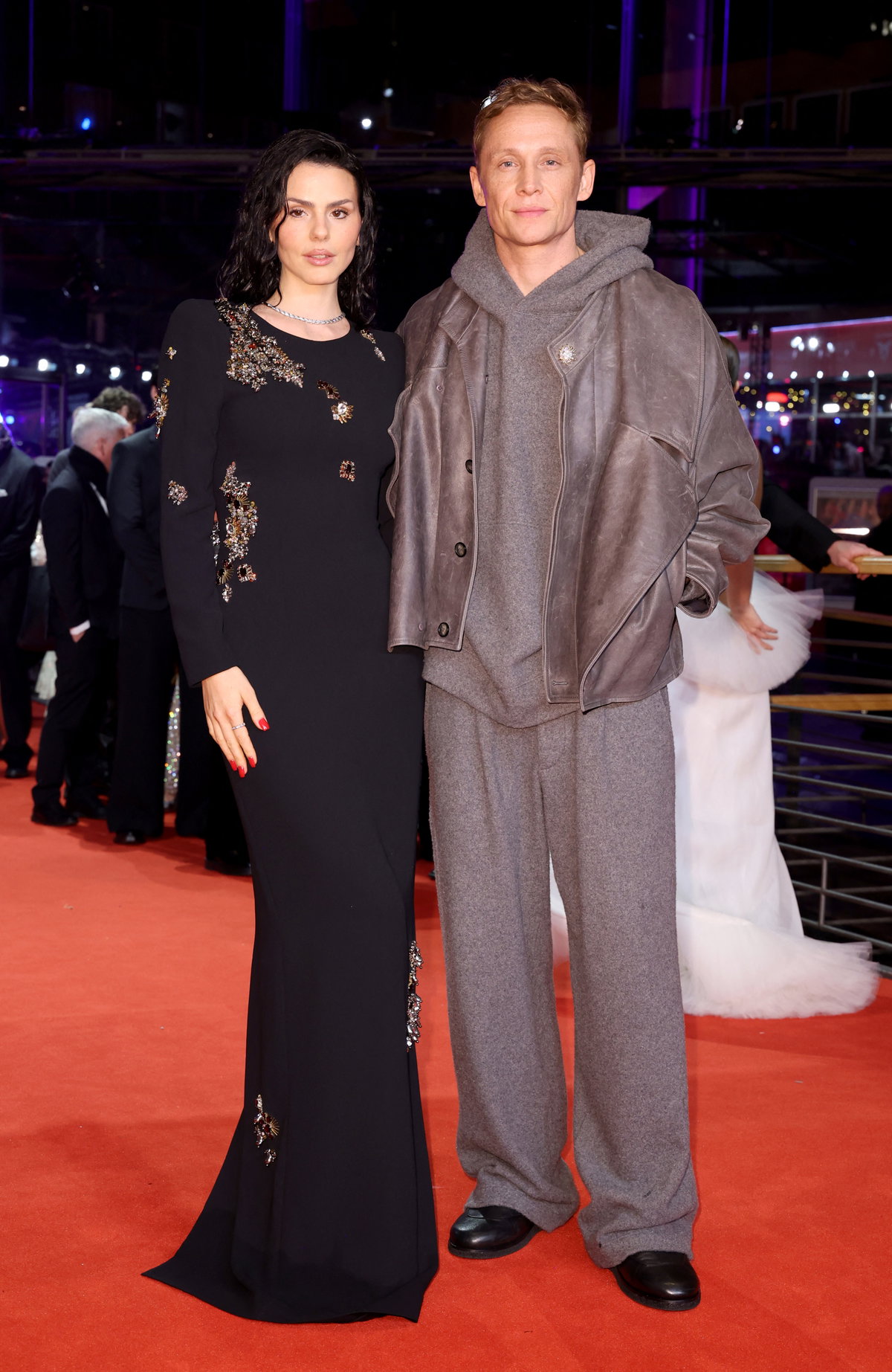 Ruby O. Fee in einem langen schwarzen Kleid mit Bestickungen und Matthias Schweighöfer in einem taupefarbenen Jogginganzug.