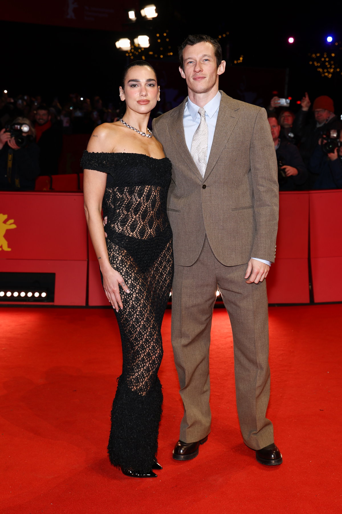 Dua Lipa in einem schwarzen Spitzenkleid und Callum Turner in einem braunen Anzug.