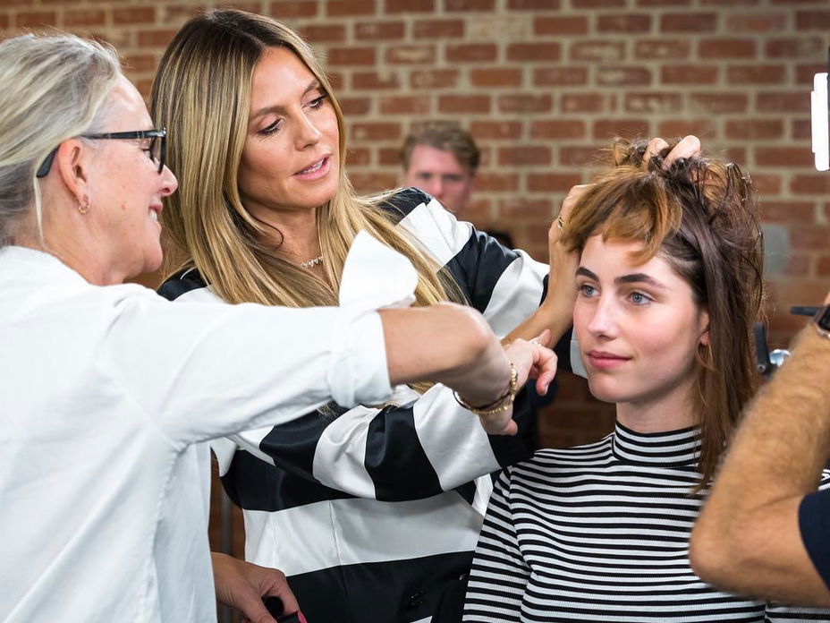 Am Set von Germany's Next Topmodel beim Umstyling steht Heidi Klum mit einer Friseurin bei einer Kandidatin.