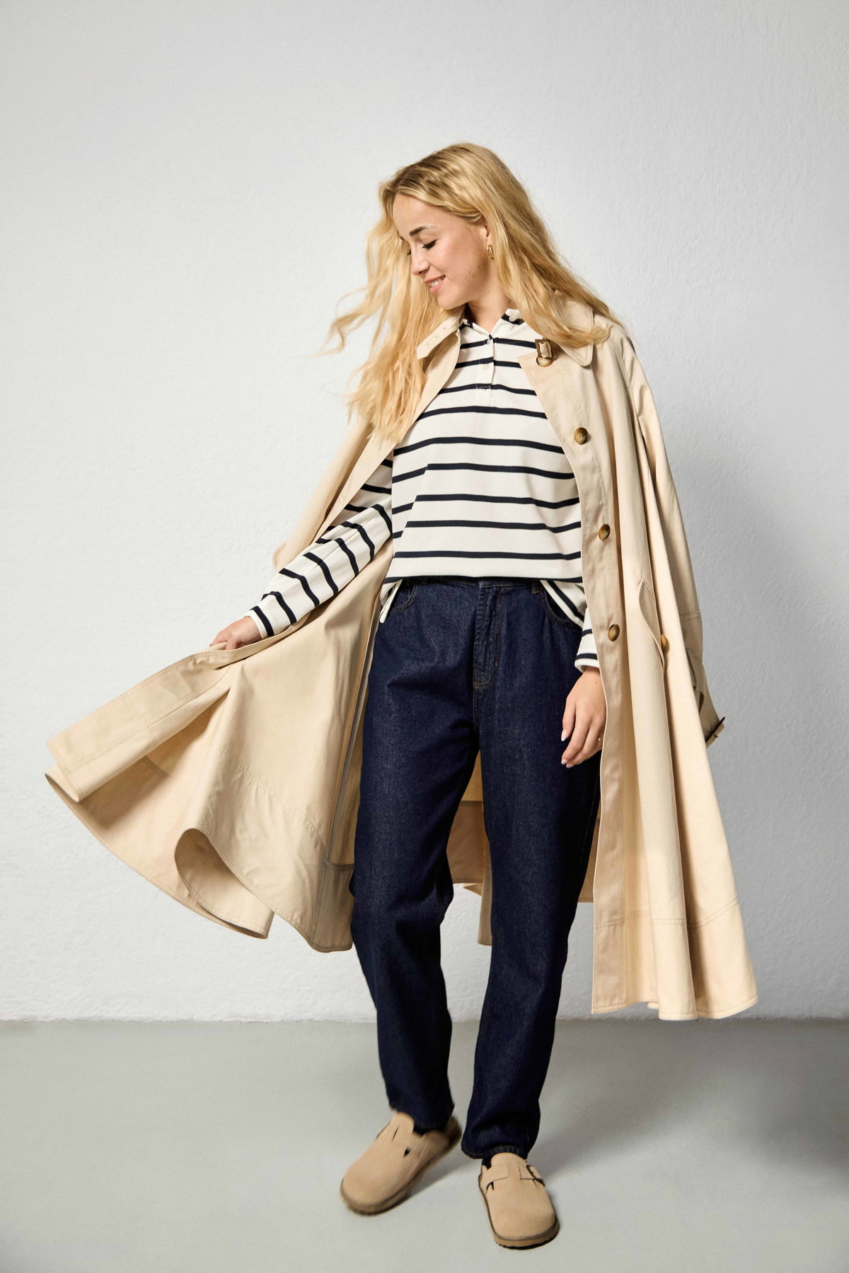Head-to-toe-Look in TK Maxx: Ausgestellter Trenchcoat, Marinière im Polo-Stil, High-Waist-Jeans, Pantoletten, Ohrringe und Ringe von TK Maxx.