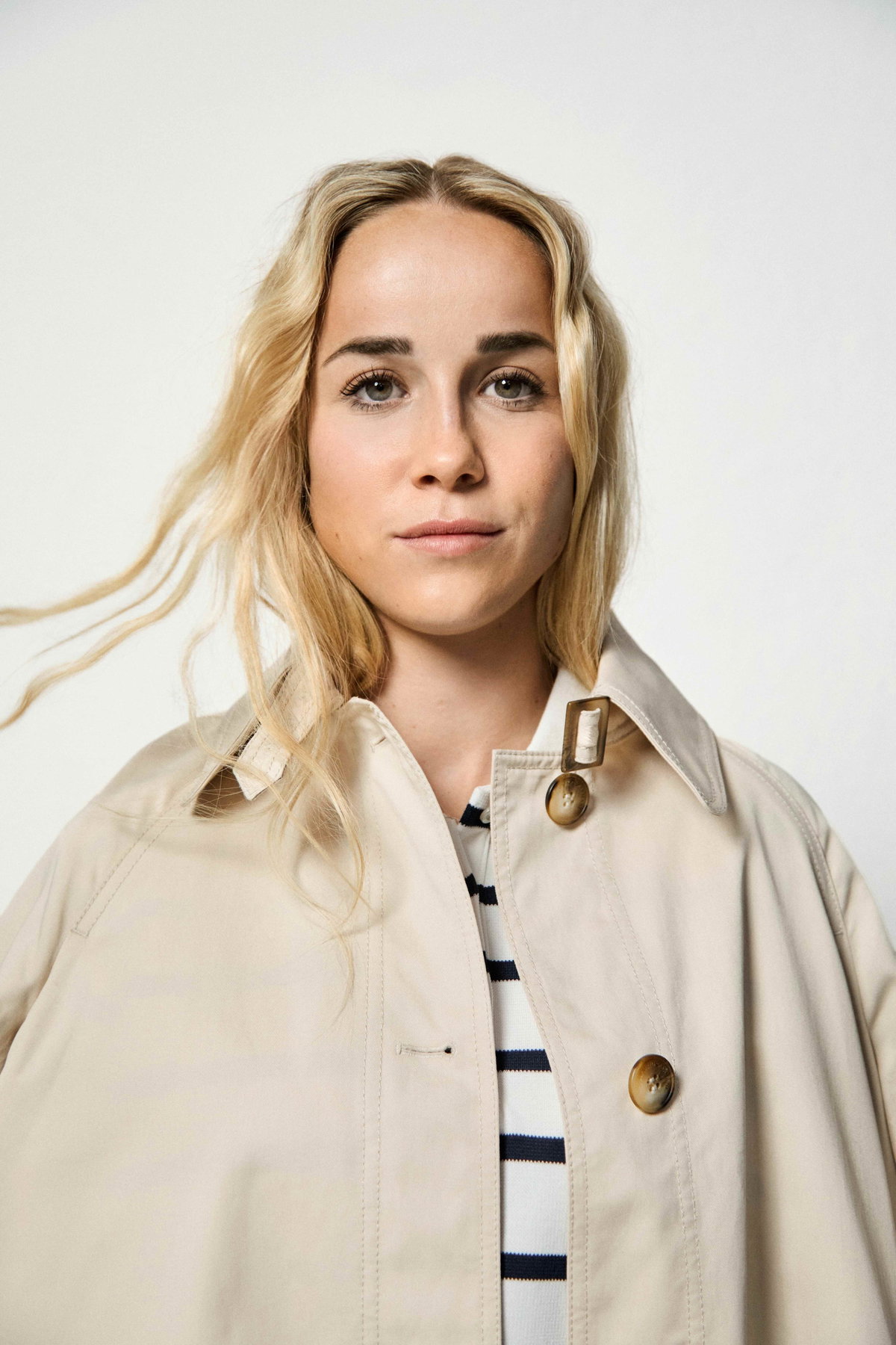 Der „casual-elegant“-Look von TK Maxx ist genau Giulias Stil: Ausgestellter Trenchcoat, Marinière im Polo-Stil, High-Waist-Jeans, Pantoletten, Ohrringe und Ringe von TK Maxx.