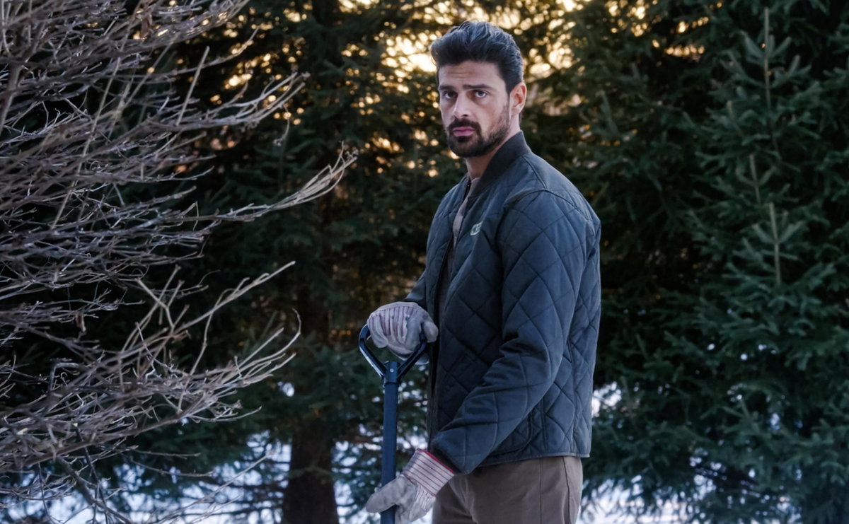 Michele Morrone im Garten mit Handschuhen, einer Steppjacke und einem Sparten.