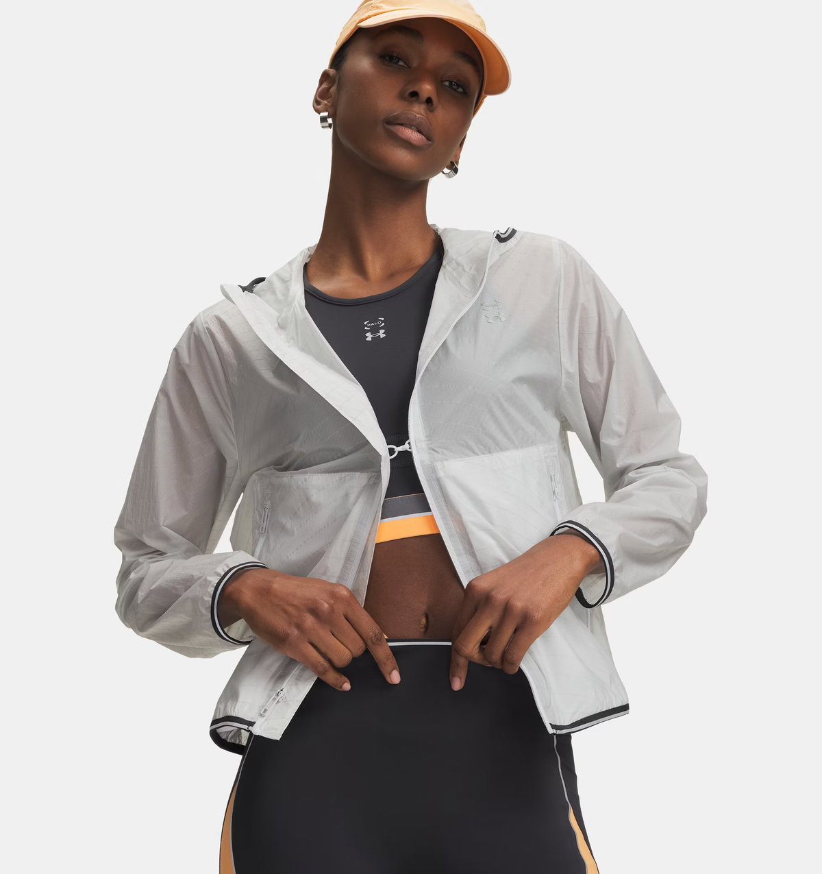 Dunkelhäutige Frau trägt Sportkleidung und eine Kappe sowie eine transparente Laufjacke.