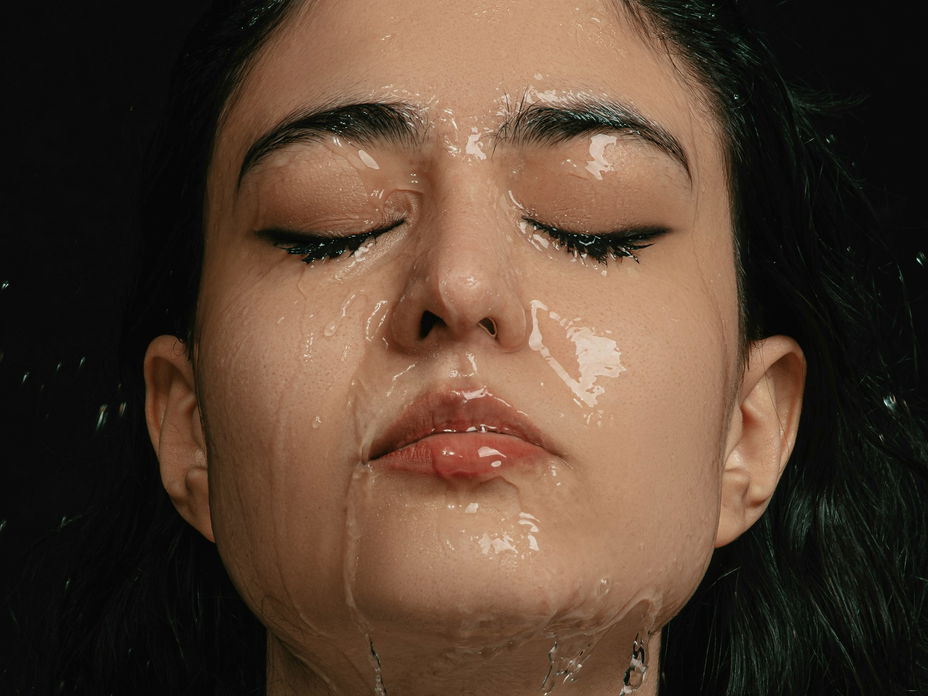 Einer Frau mit geschlossenen Augen läuft Wasser über das komplette Gesicht.