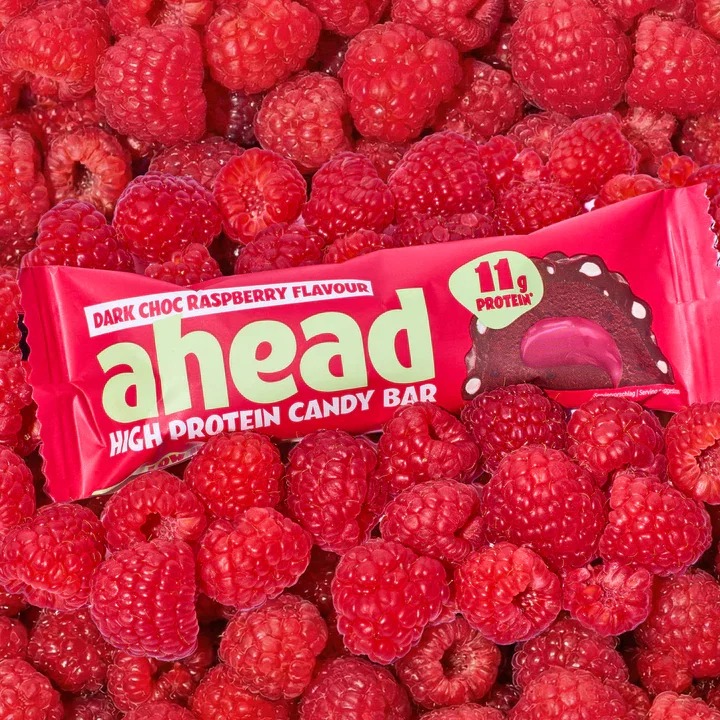 Dark Chocolate Raspberry High Protein Candy Bar von Ahead liegt auf Himbeeren.