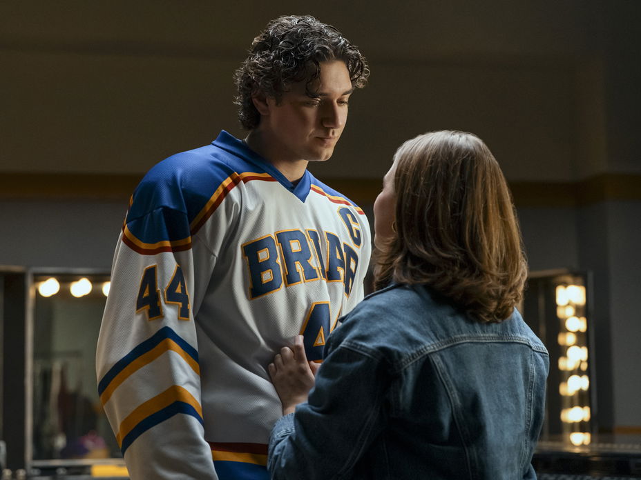 Ein junger Mann im Eishockey-Trikot steht einer jungen Frau in Jeansjacke gegenüber und guckt zu ihr herunter.