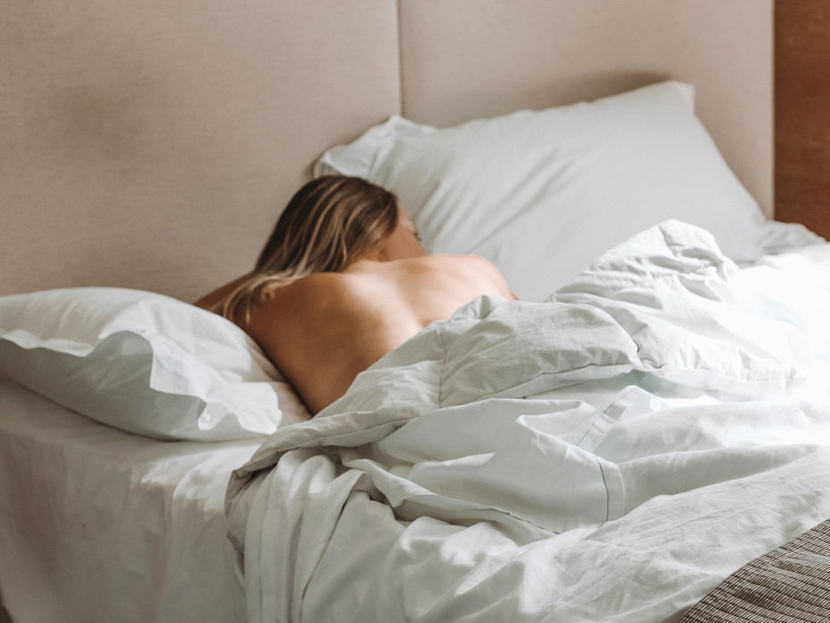 Frau liegt unbekleidet im Bett