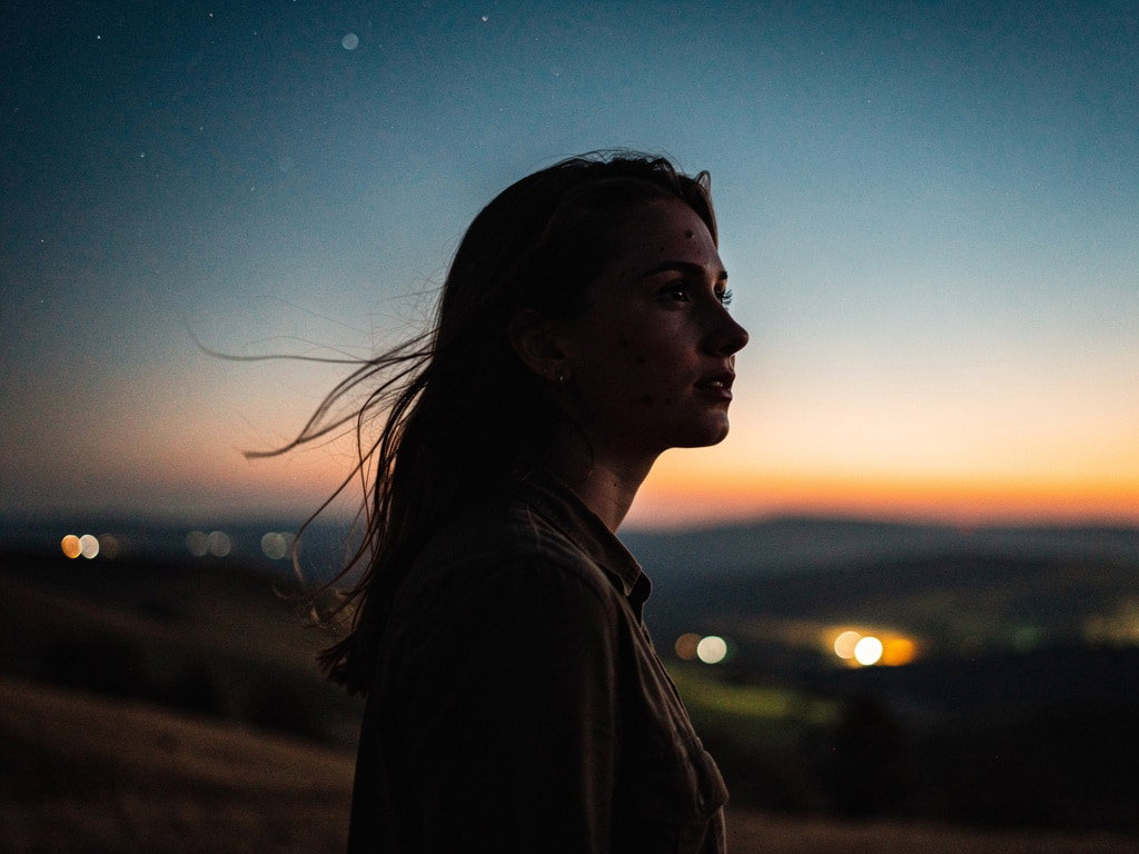 Silhouette einer jungen Frau in Landschaft mit Sternen am Himmel bei Dämmerung