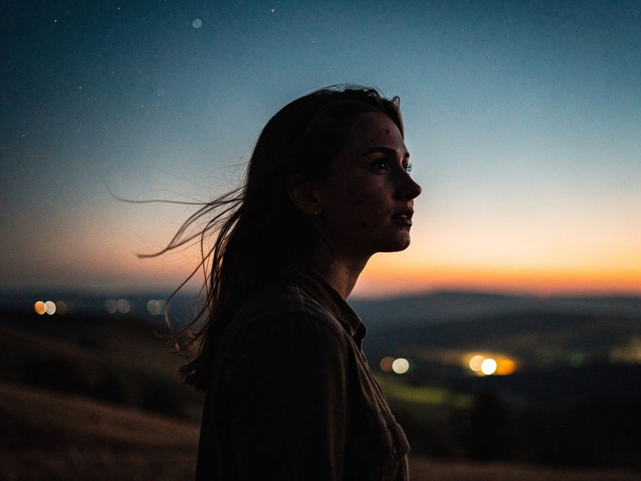 Silhouette einer jungen Frau in Landschaft mit Sternen am Himmel bei Dämmerung